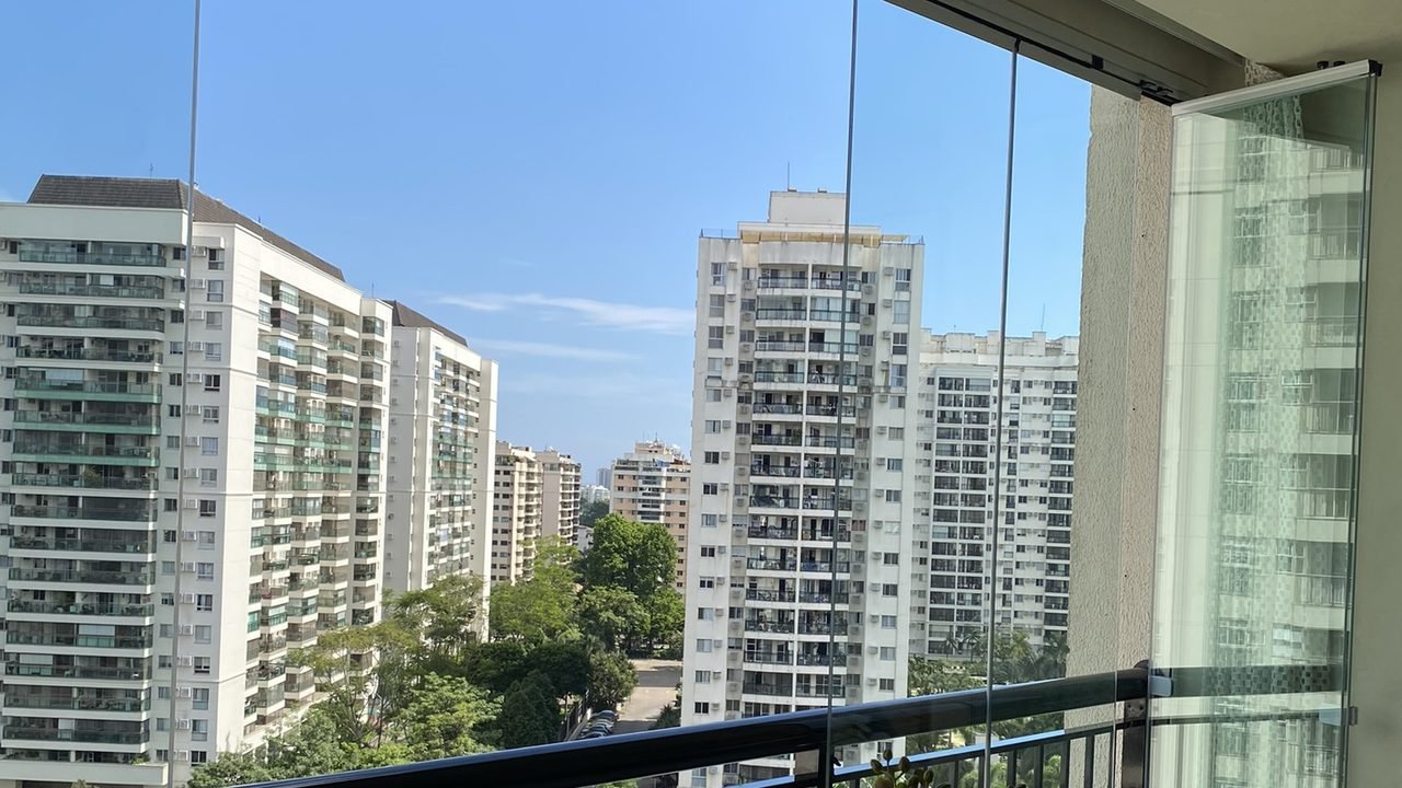 Varanda envidraçada com cortina de vidro, vista para prédios e arborização